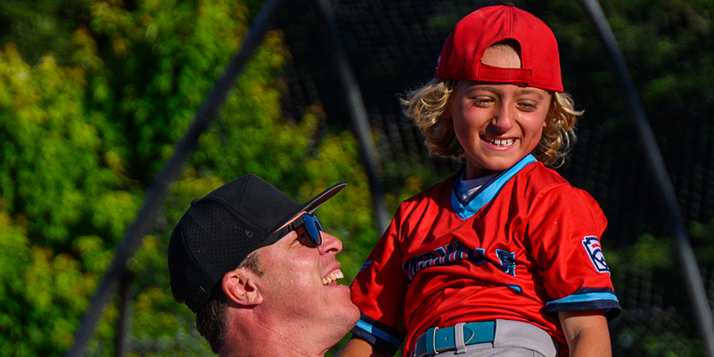 Child on father's shoulders wearing a Little League uniform
