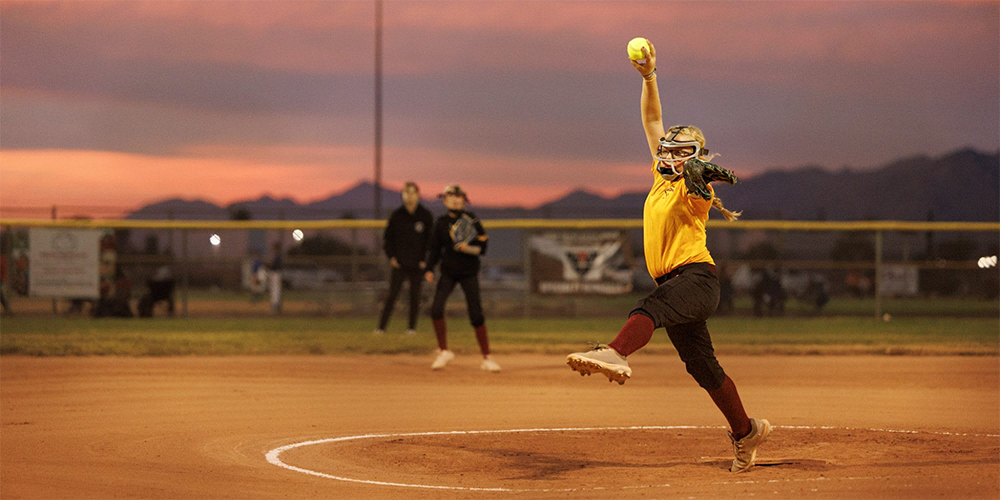 Softball pitcher pitching with a sunset background