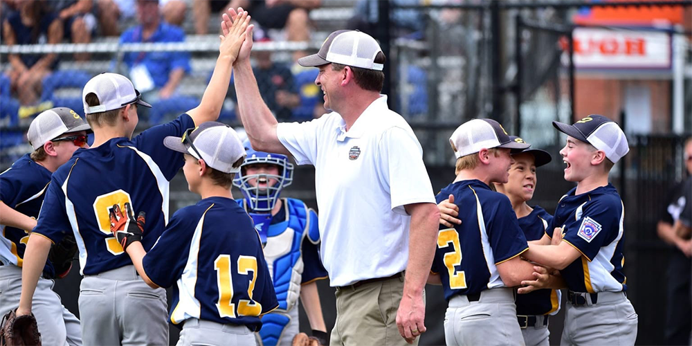 Coach high-fiving a Little League player while the rest of the team celebrates